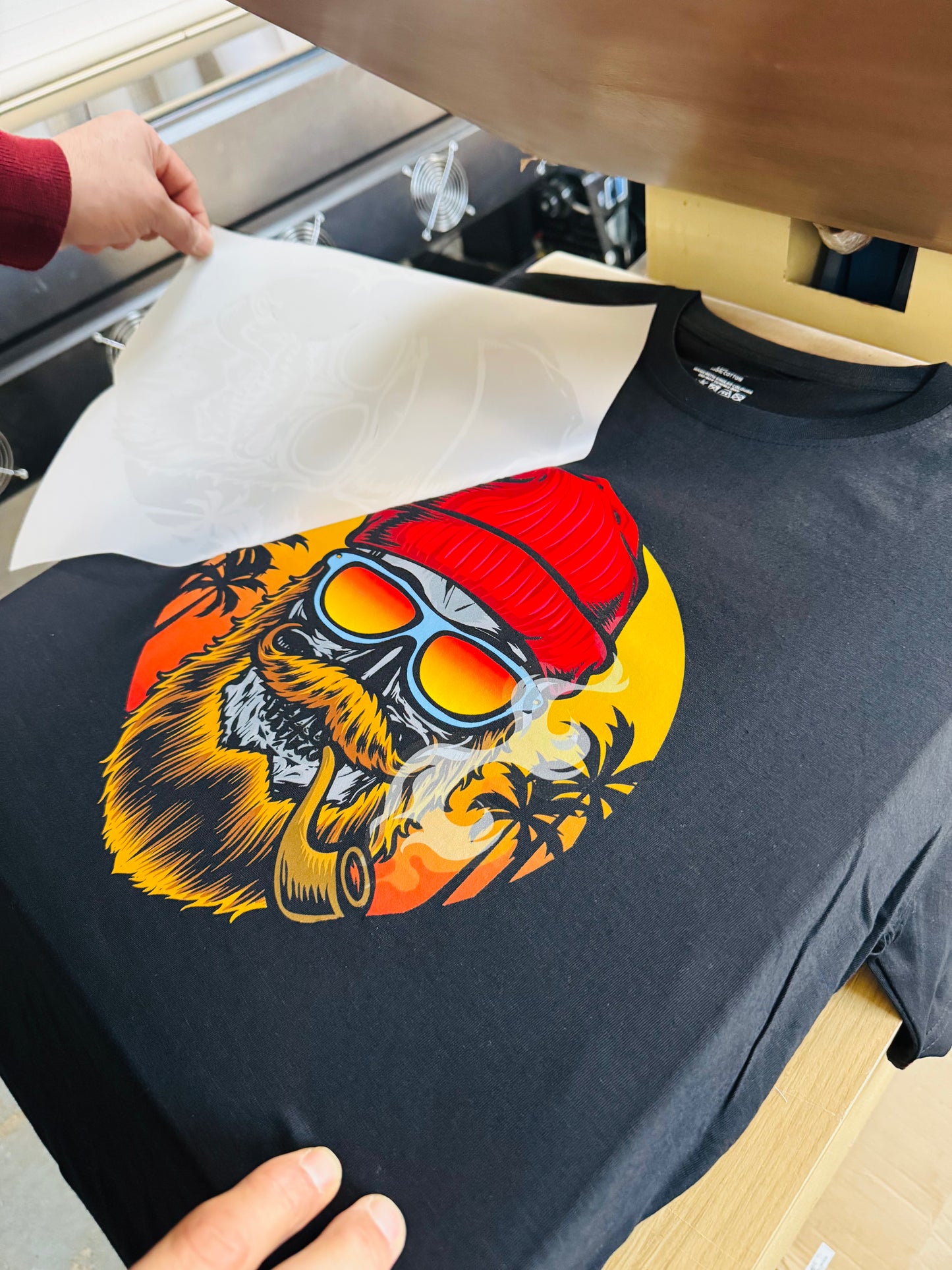 Black t-shirt with a colorful graphic of a bear wearing a red hat and sunglasses on an ironing board.