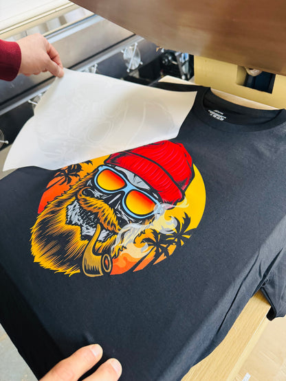 Black t-shirt with a colorful graphic of a bear wearing a red hat and sunglasses on an ironing board.