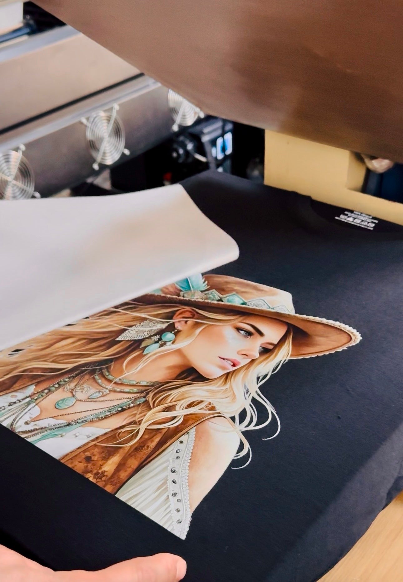 Person holding a printed t-shirt with a design of a woman wearing a hat and jewelry.