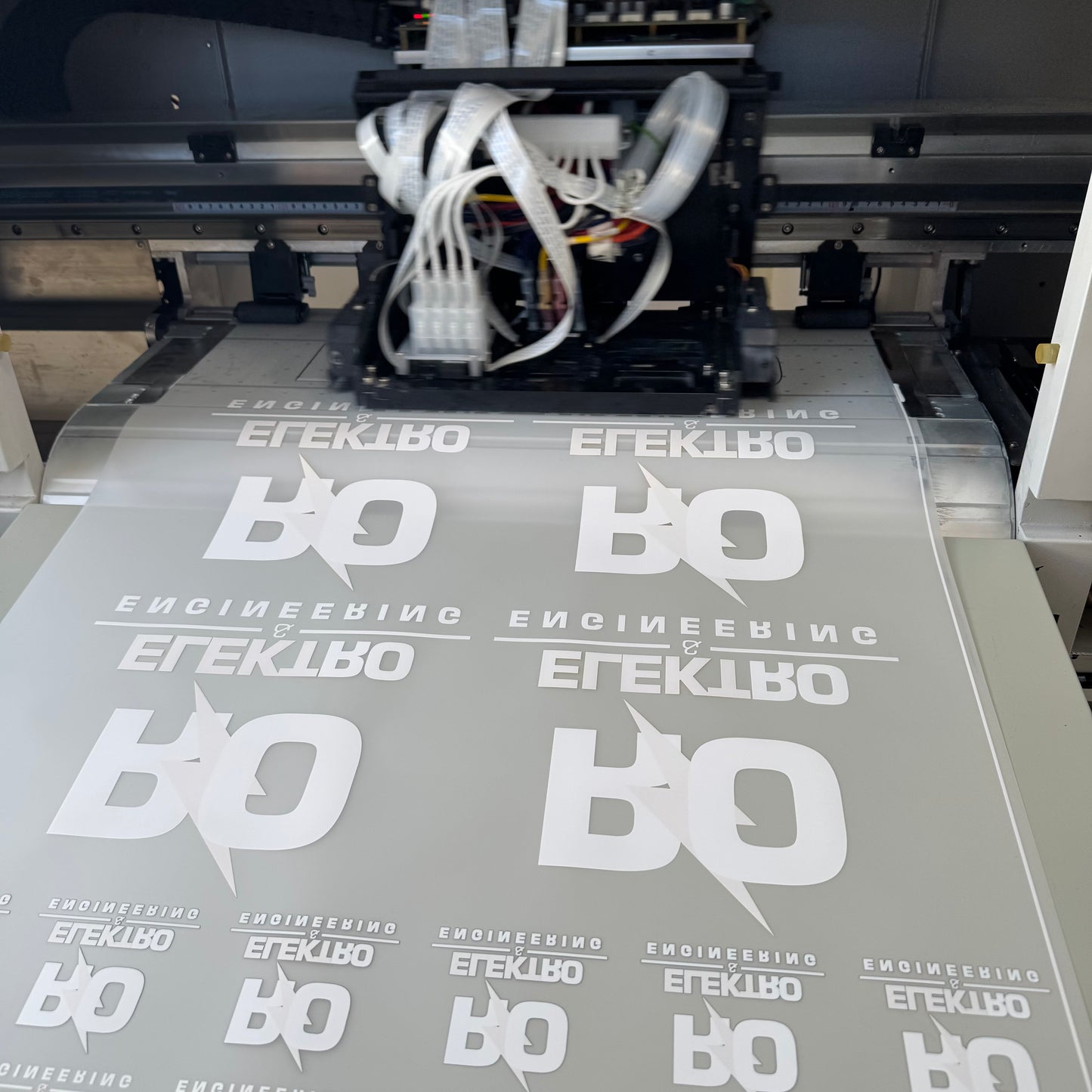 Printing process with a machine applying white text and logo onto gray material.