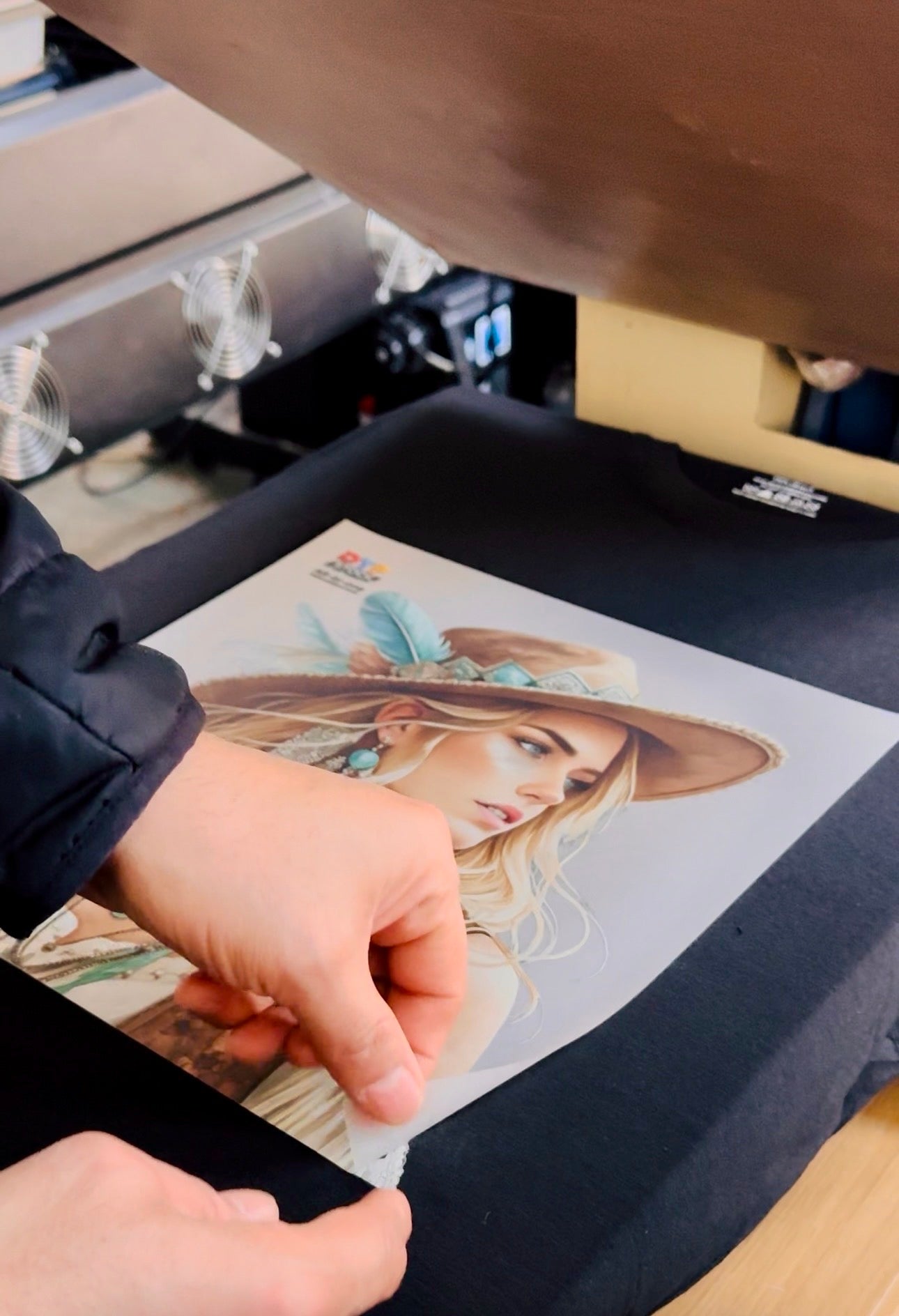 Person holding a printed design of a woman with a hat in front of a printing machine.